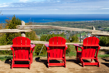 Fototapeta na wymiar View of 3 red muskoka chairs with Blue Mountain resort and village and Lake Huron Georgian Bay at the background during the autumn in Collingwood, Ontario