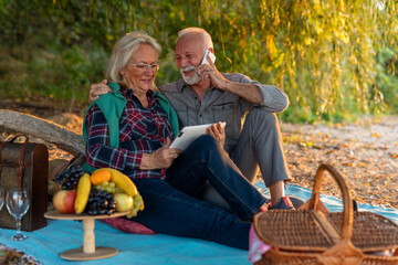 Portrait of an elderly couple sitting and looking at tablet by the river.