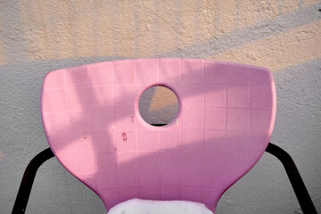 Pink and vintage retro style seat with metal and black supports. Sunshine on seat and wall behind it during winter and some amount of white snows on seat. 