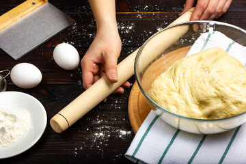 The process of making butter dough. Rolling pin for dough in female hands. Yeast dough in a glass bowl. Rustic bread baking.
