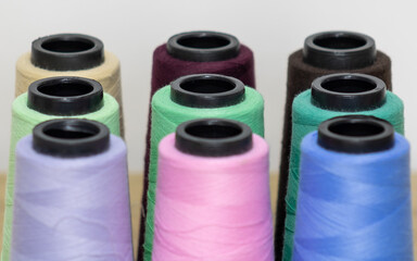 Nine sewing threads with different shades on their spools aligned horizontally on a table with a...