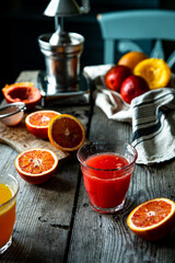 Glass of fresh blood orange juice, orange halves and juicer machine on wooden table with chair on background .