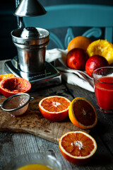 Blood orange halves with fresh juice in glasses and juicer machine on background on wooden table.