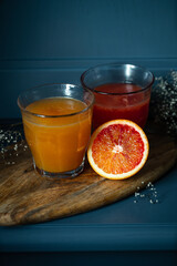 Two glasses of fresh orange and  blood orange juice  on wooden board on Prussian blue background.