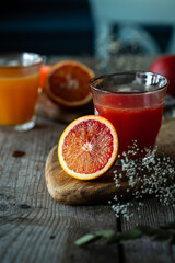 Glass of fresh blood orange juice sand blood orange half on wooden table .