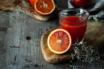 Glass of fresh blood orange juice sand blood orange half on wooden table .