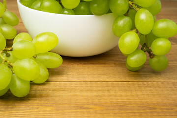 Green grapes in white ceramic bowl on wooden table, close up.