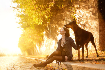 Girl with doberman. Beautiful young woman with dog at the sunset time at the street.