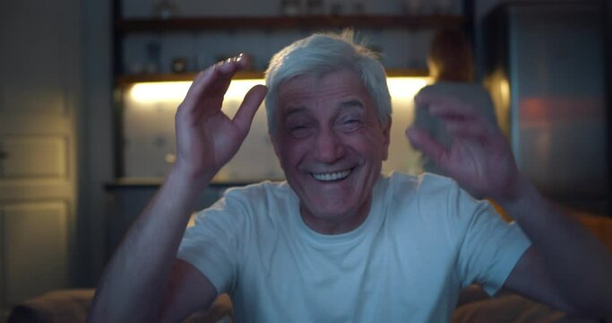 Close up of aged man watching tv in evening and laughing relaxing on couch
