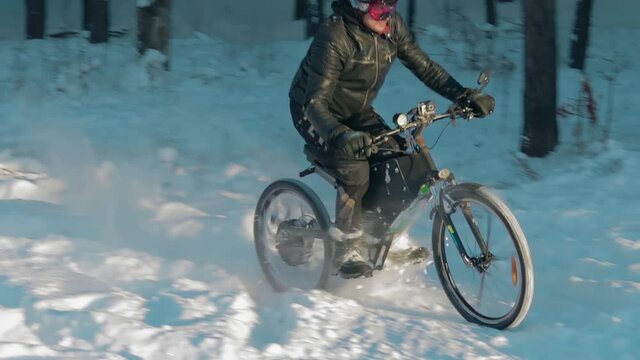 Cyclist in Black Clothes, Helmet and Snow Glasses Riding on Electric Bike in the Snow in Winter Forest. E-Bike Riding and Drifting at Cold Sunny Day - Slow Motion