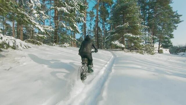 Cyclist in Black Clothes, Helmet and Snow Glasses Riding on Electric Bike in the Snow in Winter Forest. E-Bike Riding and Drifting at Cold Sunny Day - Super Slow Motion
