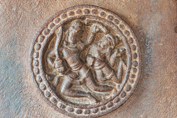 Aihole, Karnataka, India - November 7, 2013: Durga Gudi or Temple. Closeup of brown stone, 2 human figures sculpture captured in circular decoration but faces damaged.