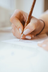 A hand with pen creates a business card with a calligraphic letter
