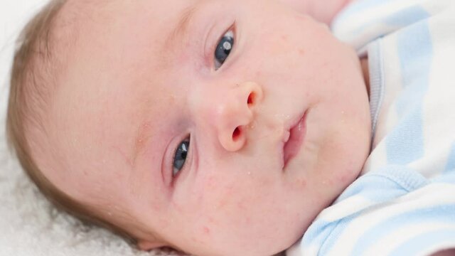 Closeup slow motion portrait of newborn baby boy with blue eyes lying on soft blanket on changing table. Concept of babies and newborn hygiene and healthcare. Caring parents with little children.