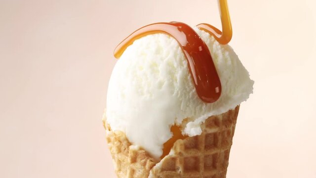 melted caramel sauce flowing on rotating vanilla ice cream in waffle scoop close up