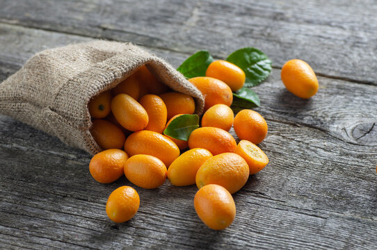Fresh ripe kumquat fruits in burlap sack on wooden background, fortunella margarita