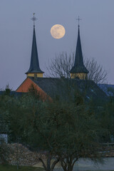 Full moon in between two church towers in the blue evening sky