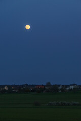 Full moon over rural landscape at blue hour outside village