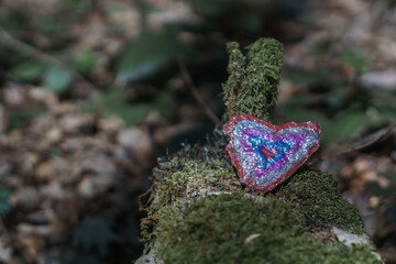 heart shaped stone painted colorful lying on a mossy dead tree trunk
