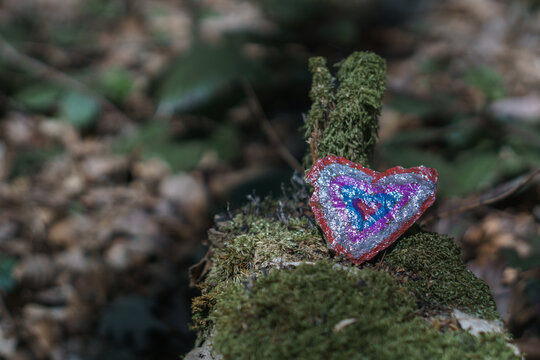 heart shaped stone painted colorful lying on a mossy dead tree trunk - Powered by Adobe