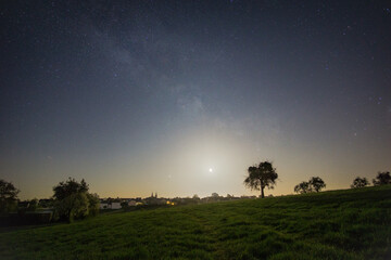 crescent moon and milkyway over meadow with trees outside a german village in the eifel