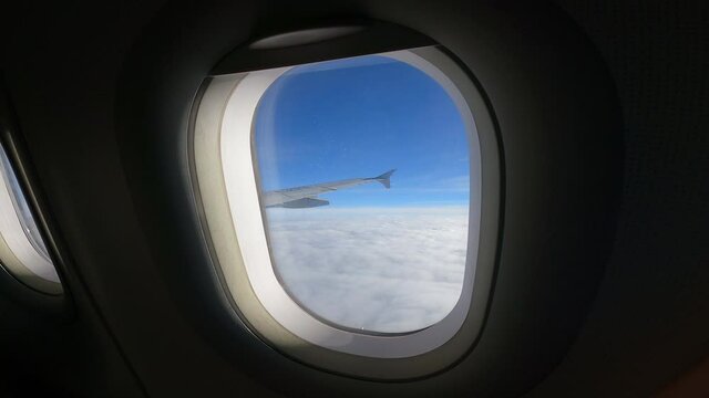View of beautiful clouds and wing of airplane from window, airplane window with cloudy sky behind. Royalty high-quality free stock video footage looking through window aircraft during flight in wing w