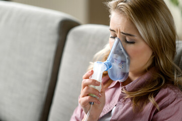 Close-up photo of sick caucasian woman with an inhaler. Unhealthy female doing inhalation at home, she use nebulizer and inhaler for the treatment sitting on the couch at home