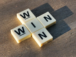Side view WIN WIN crossword by square letter tiles against wooden background.