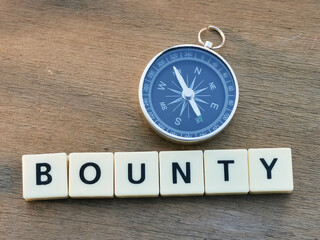Top view BOUNTY crossword by square letter tiles against wooden background with compass.