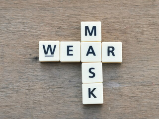 Top view WEAR MASK crossword by square letter tiles against wooden background.Medical concept.