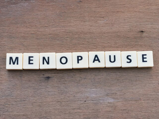 Top view MENOPAUSE crossword by square letter tiles against wooden background.Medical concept.