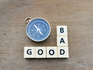 Top view GOOD BAD crossword by square letter tiles against wooden background with compass.