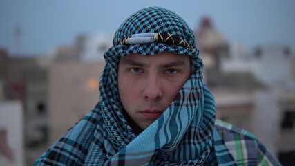 A young man in an Arab handkerchief. The man looks at the camera. On the roof of a house against the background of Arab houses.