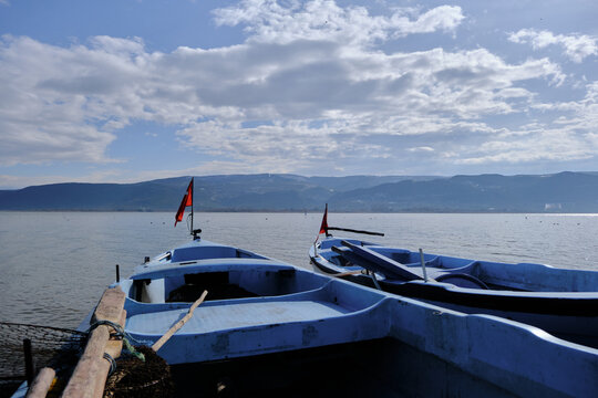 Small and blue boats near the coast of Lake of Uluabat in Turkey. Small Turkish flag on the boat with lake and mountain background. Bursa. Golyazi (Apollyon). Bursa, Turkey. 22.01.2021.