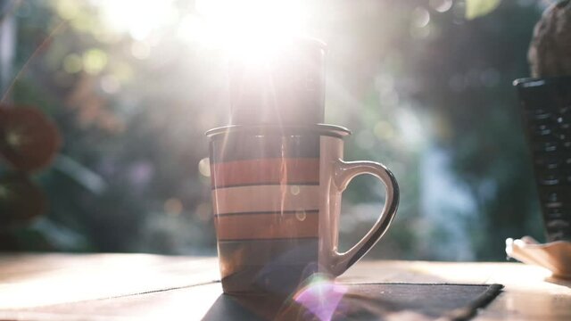 New day with a coffee in the garden. Royalty high-quality free stock footage of a cup of coffee with sunshine, sun flare. Wonderful garden with greenery and fresh air for relaxation. Amazing morning