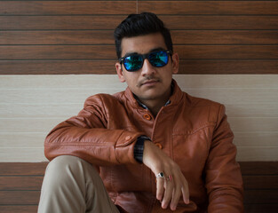 picture of indian boy wearing brown leather coat and blue sunglasses looking into camera