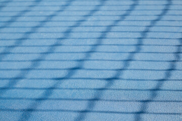 Abstract tennis court texture. Defocused tennis net shadow on ground, outside early morning. Blue...