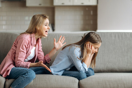 Angry mother scolding little daughter at living room, parent teaches a naughty mischievous child, kid girl feels upset about punishment and deprivation of entertainment