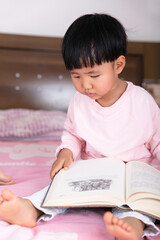 A little girl sitting in bed reading a Book
