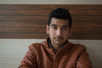 teen boy wearing brown leather coat looking into camera with smart and doubtful face