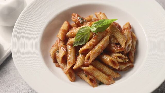 Green basil is placed on penne pasta with tomato sauce, close up 