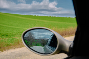 Observing of gravel road from a car rear mirror at the top of the small hill with gravel roads with magnificent cloudy sky background