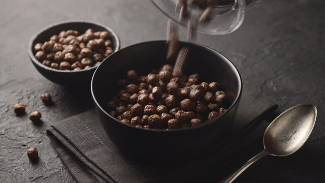 Chocolate balls for breakfast cereal are poured into a bowl, dark background, close-up 