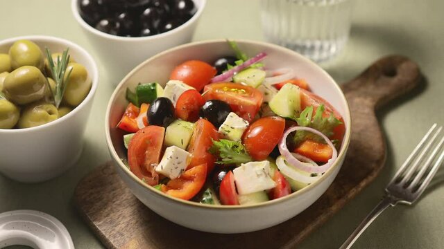 Greek salad poured with olive oil, green background, close-up 