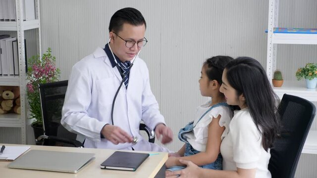 Kind male doctor with glasses, putting on stethoscope, listening to lung function from a cute girl who sitting on mother's lap, and breathing heavily. Asian pediatrician and kid concept. 