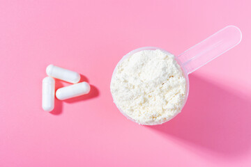 Scoop with protein powder and capsules on pink background top view.