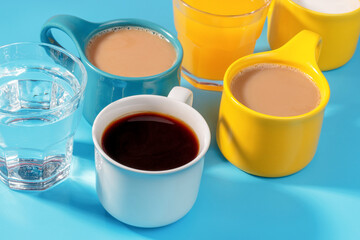 Multicolored mugs with drinks on blue background side view.