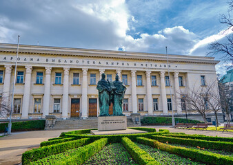 Obraz premium In front of Sts. Cyril and Methodius National Library with a statue and small park with dried trees and street on car. Bulgaria. Sofia. 06.01.2021.