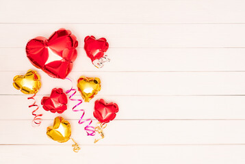 Seven metallic shiny balloons in the form of heart. One big red shiny balloon in the shape of a heart and six small heart-shaped balloons in gold and red colors with ribbons lie on wooden beige boards