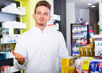 Young man pharmacist wearing uniform and working in pharmaceutical shop